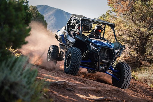 Three-quarter front angle of a person driving a side x side on a dirt trail. opens in a new window