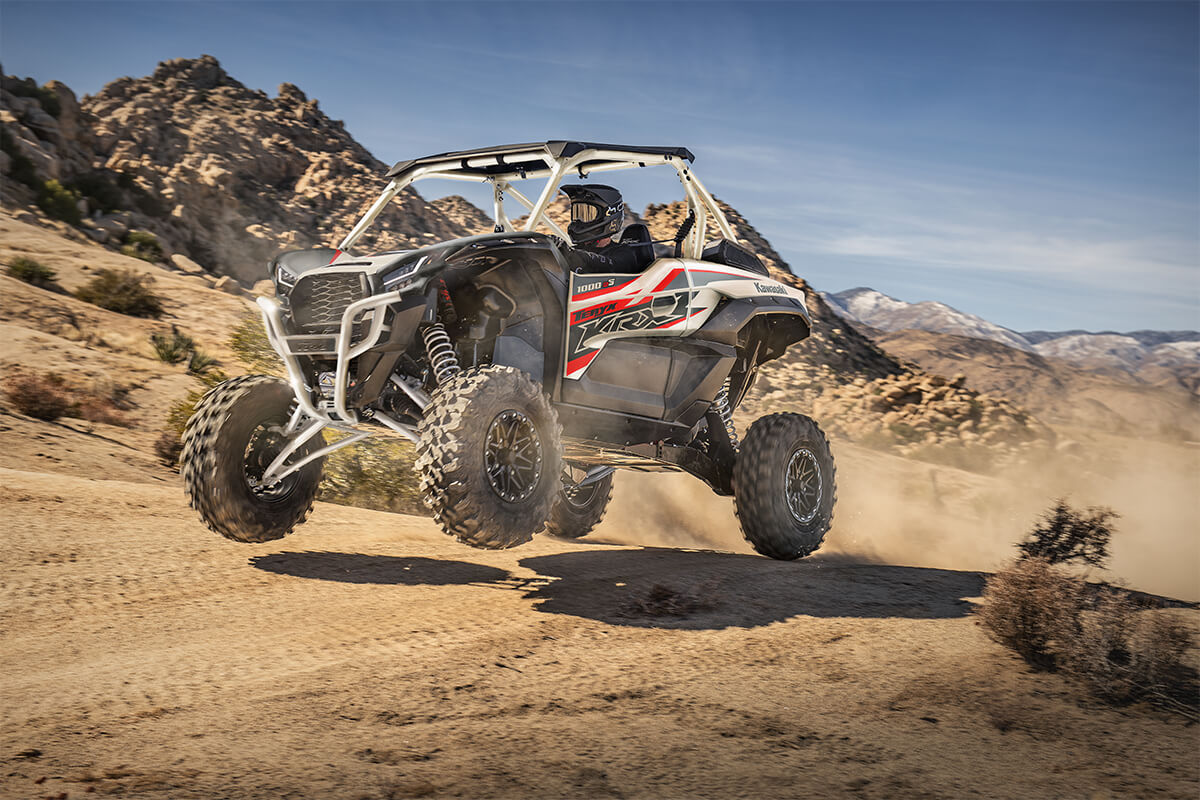 Three-quarter front angle of a person driving a side x side uphill.