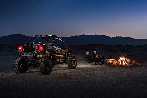 Three-quarter rear angle of a side x side off-road at night next to a bonfire. opens in a new window
