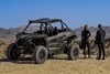 Two people standing behind a side x side parked off-road.