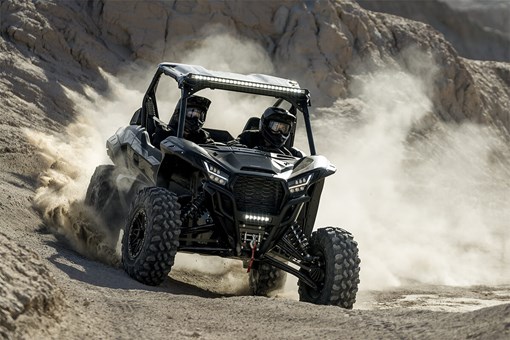Three-quarter front angle of a side x side kicking up dust off-road. opens in a new window