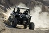 Three-quarter front angle of a side x side kicking up dust off-road.