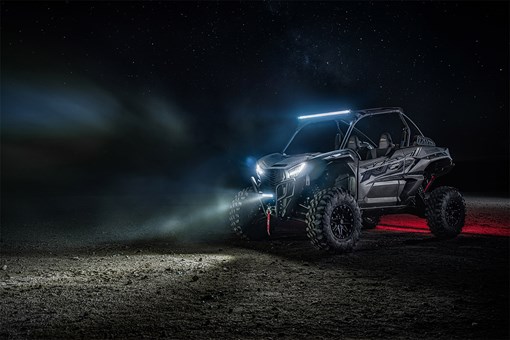 Three-quarter front angle of a side x side with lights on parked off-road at night. opens in a new window