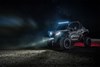 Three-quarter front angle of a side x side with lights on parked off-road at night.