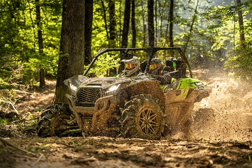 Three-quarter front angle of a side x side kicking up mud off-road. opens in a new window