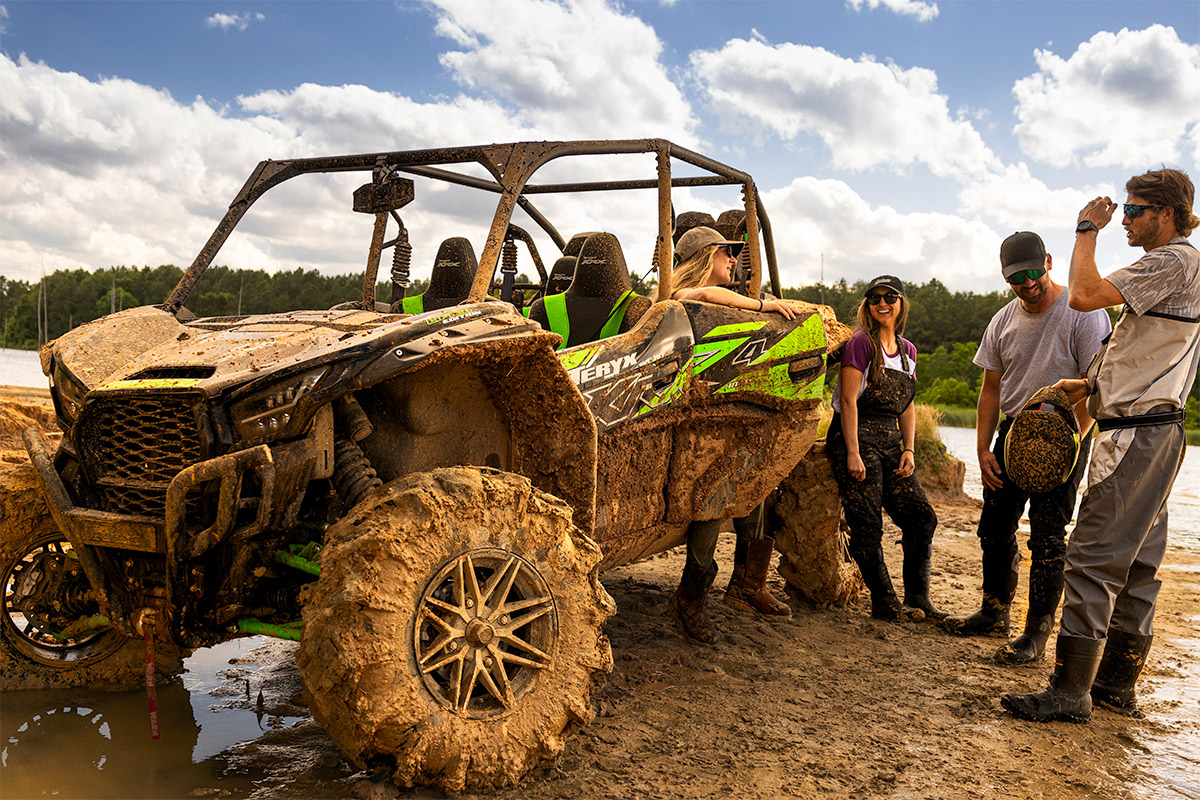 A group of people talking next to a side x side parked off-road.