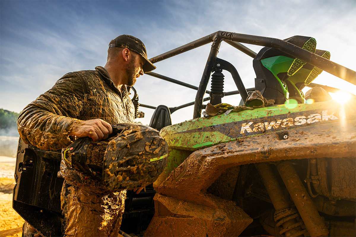 A rider standing next to a side x side parked off-road.