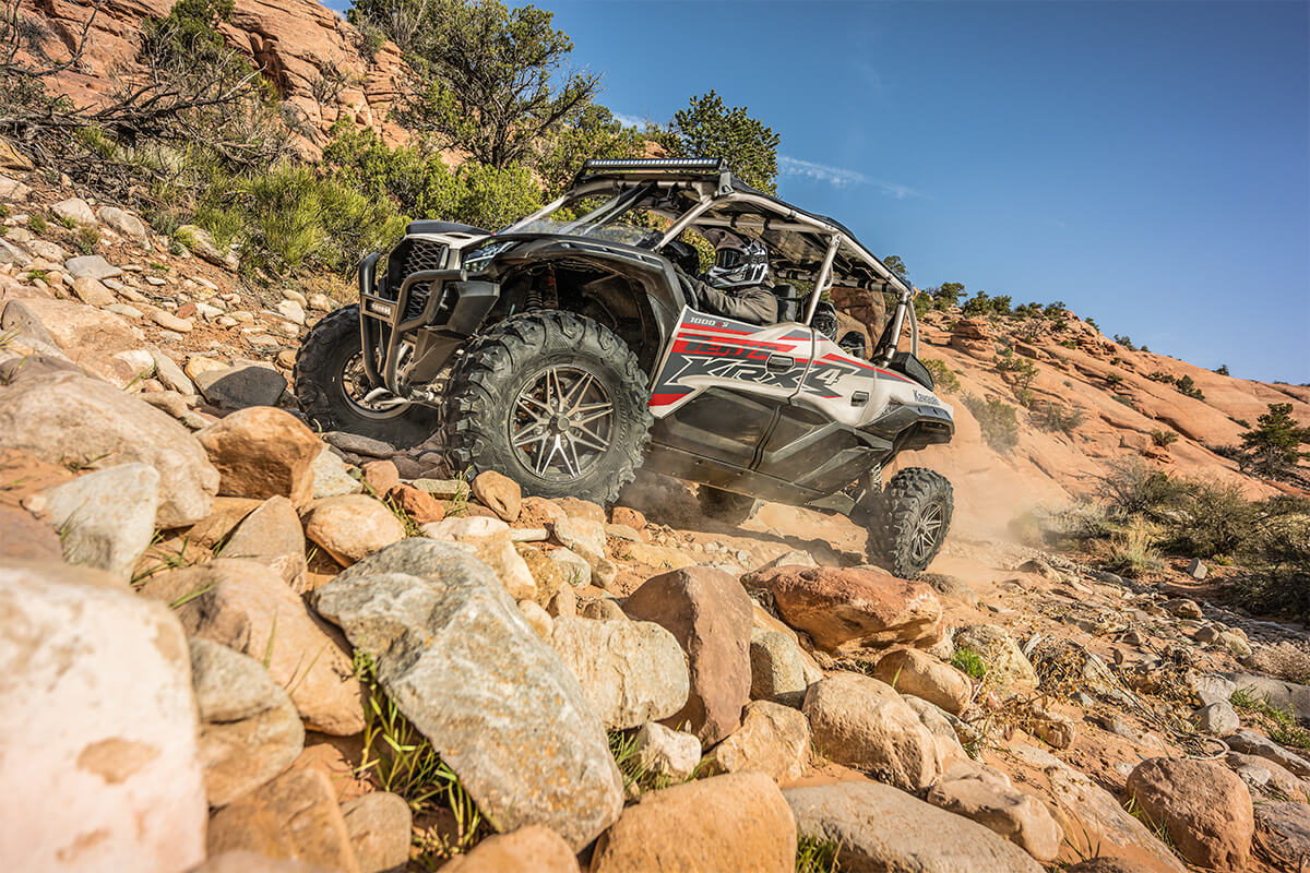 Three-quarter front angle of a person driving a side x side up a rocky hill.