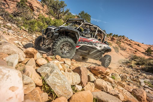 Three-quarter front angle of a person driving a side x side up a rocky hill. opens in a new window