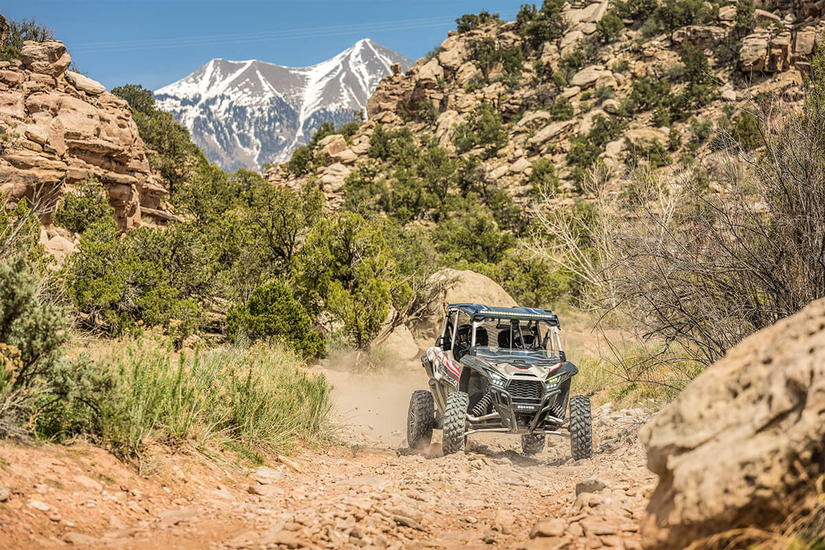 Three-quarter front angle of a person driving a side x side on a dirt trail.