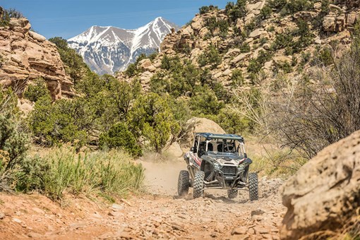 Three-quarter front angle of a person driving a side x side on a dirt trail. opens in a new window
