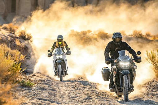 Front angle of two motorcycles riding off-road with dust in the background. opens in a new window