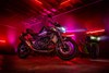 Side angle of a motorcycle staged in a warehouse with neon lights.
