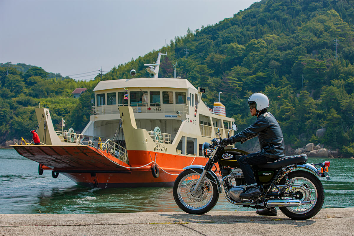 Side angle of a person seated on a motorcycle in front of a ferry boat.