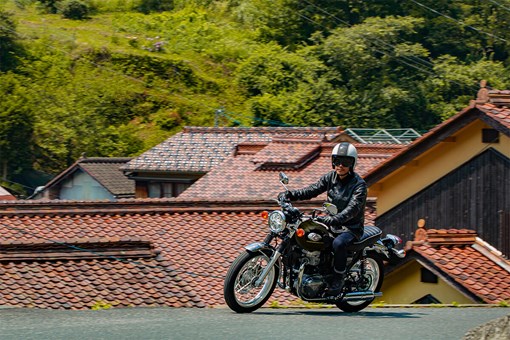 Three-quarter front angle of a person riding a motorcycle on a village road. opens in a new window
