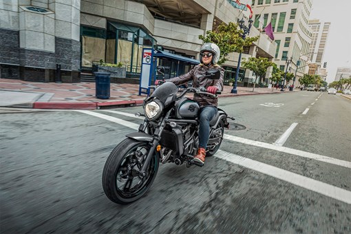 Three-quarter front angle of a person riding a motorcycle on a city street. opens in a new window
