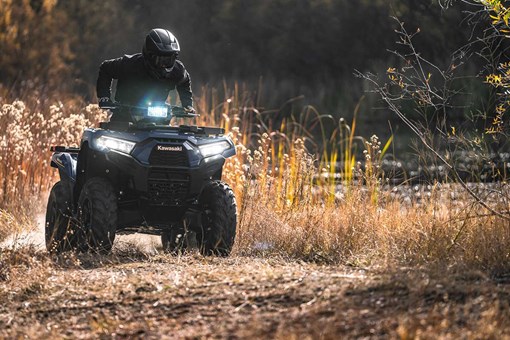 Front view of a person riding an ATV off-road with the headlights on. opens in a new window