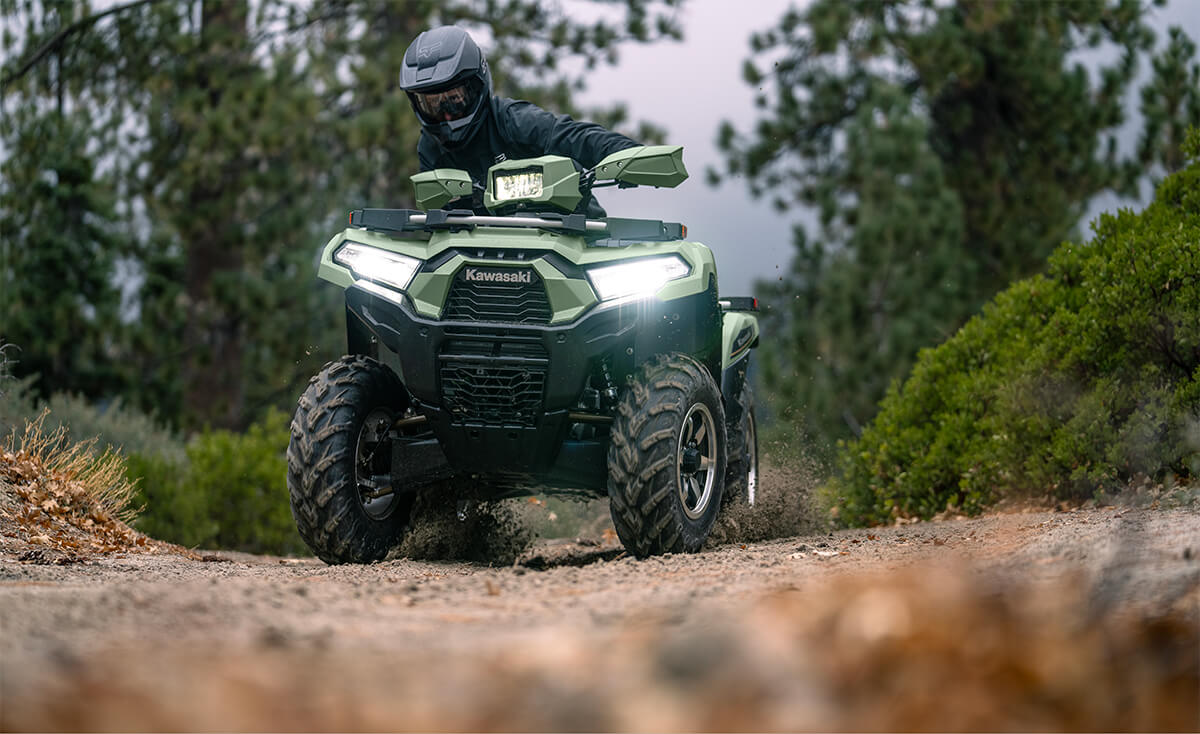 Front view of a person riding an ATV off-road with headlights on.
