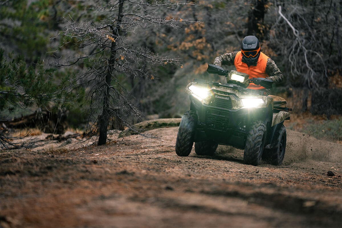 Front view of a person riding an ATV off-road with headlights on.