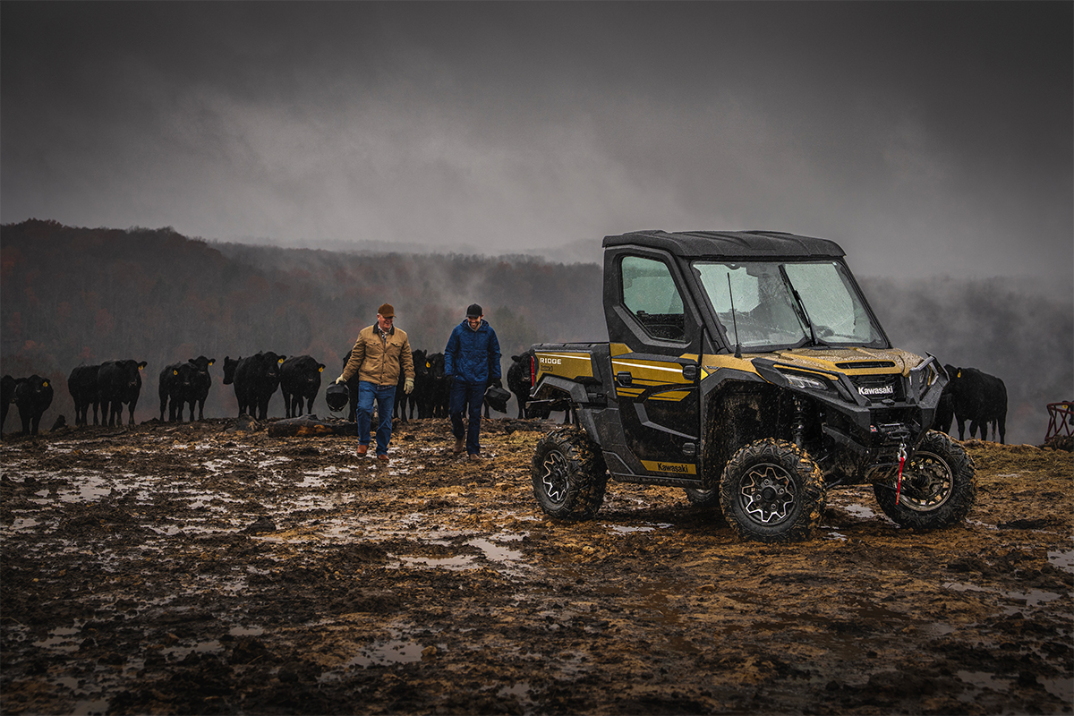 Front three-quarter view of a side x side parked next to ranchers and a herd of cattle.