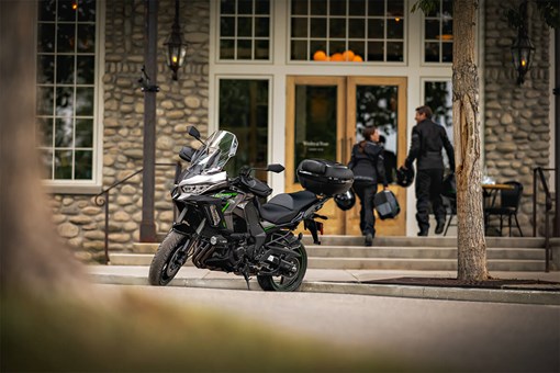 Side angle of a parked motorcycle with people in the background entering a building. opens in a new window