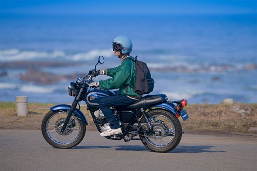 Side angle of a person seated on a motorcycle on a roadway. opens in a new window