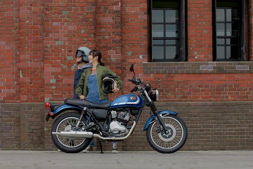 Side angle of two people standing near a parked motorcycle. opens in a new window