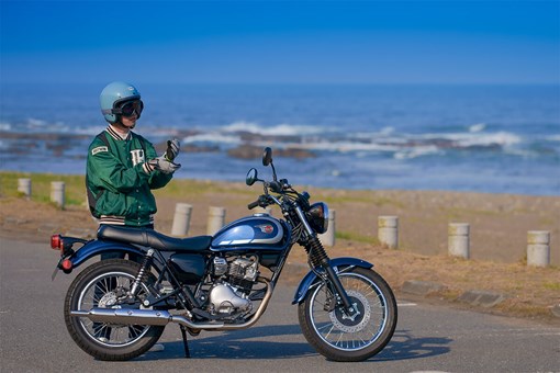 Side angle of a person standing near a parked motorcycle. opens in a new window