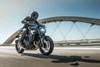 Side angle of a person riding a motorcycle on a bridge.