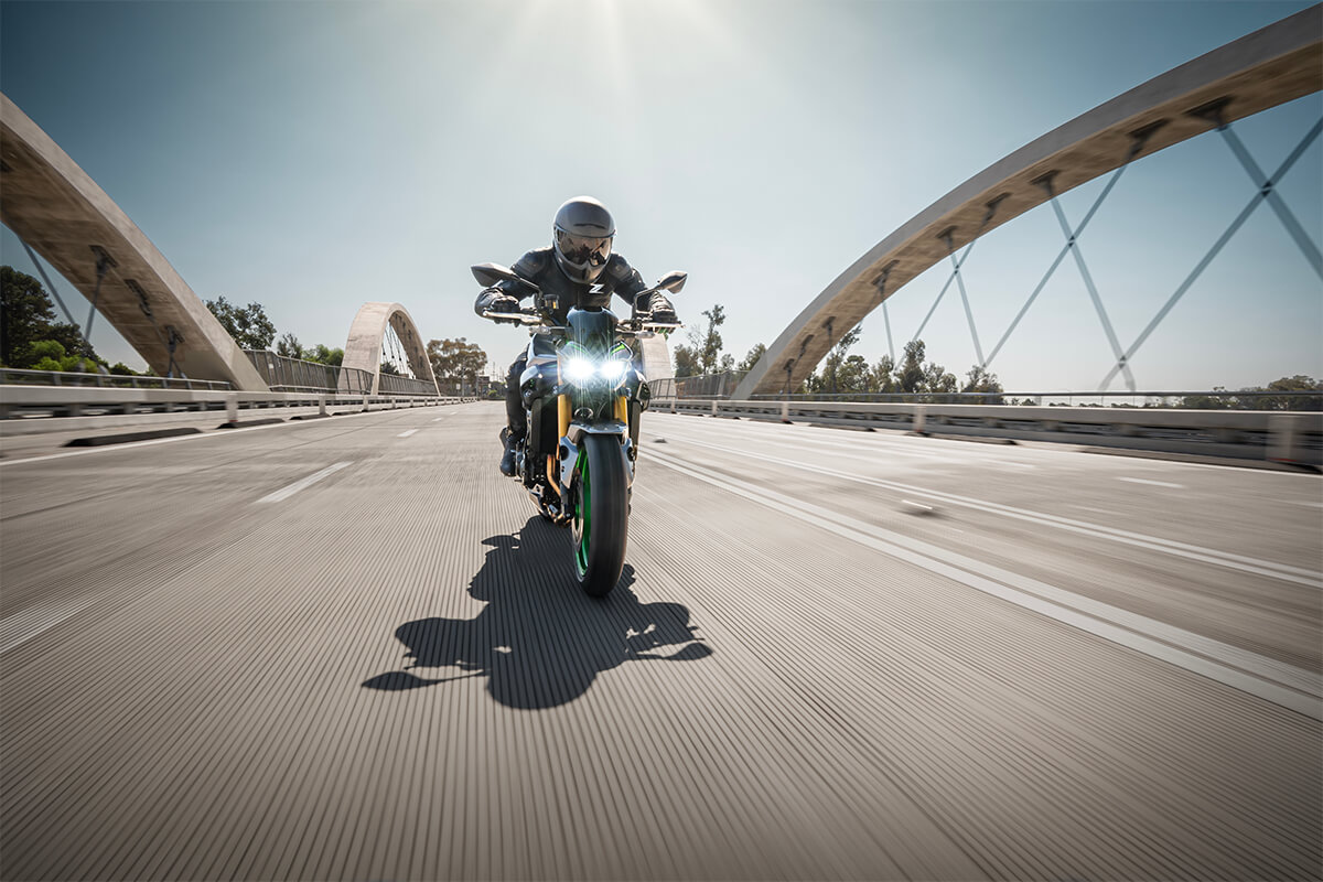 Front angle of a person riding a motorcycle on a bridge.