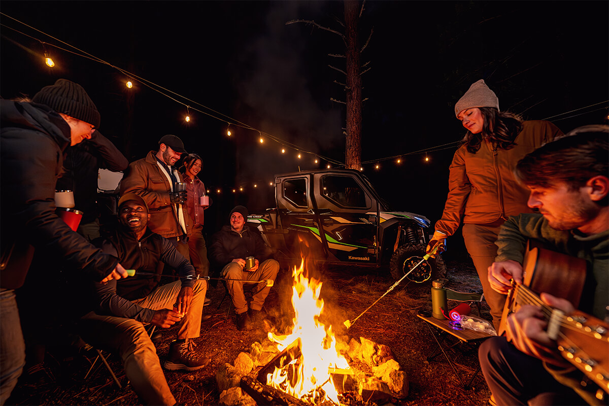 Campfire scene with people and a side x side in the background.