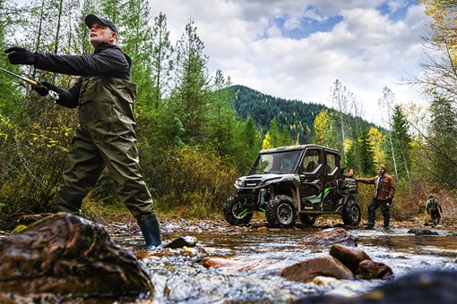 Front three-quarter view of a side x side at a river next to fly fishermen. opens in a new window