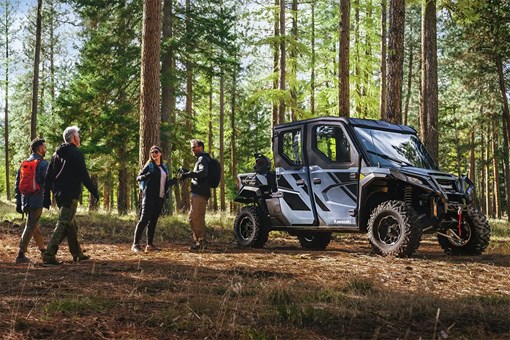 Front three-quarter view of a side x side in the woods next to hikers. opens in a new window