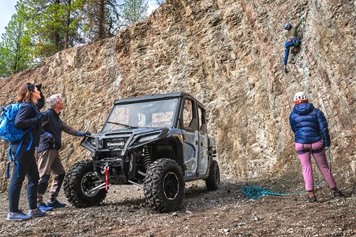 Front three-quarter view of a side x side next to rock climbers. opens in a new window