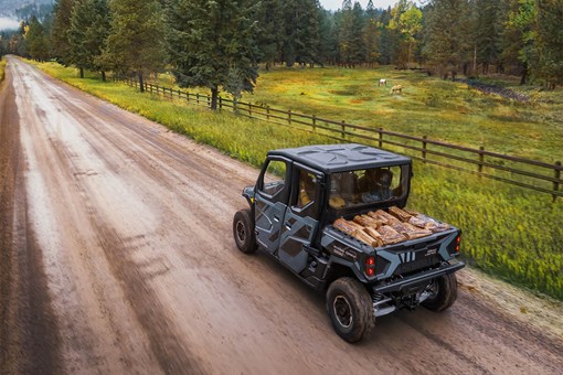 Side x side with four people and a cargo bed full of firewood on a dirt road. opens in a new window