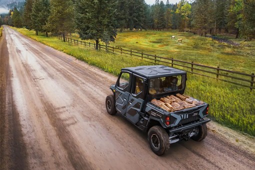 Side x side with four people and a cargo bed full of firewood on a dirt road. opens in a new window