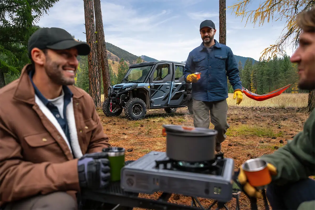 Men having coffee in a campground with a side x side in the background.