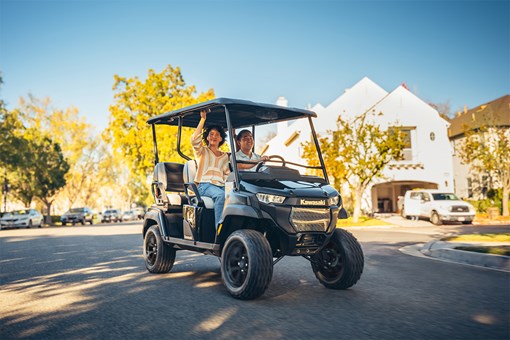 Three-quarter front angle of two people riding in a Neighborhood Activity Vehicle on a community roadway. opens in a new window