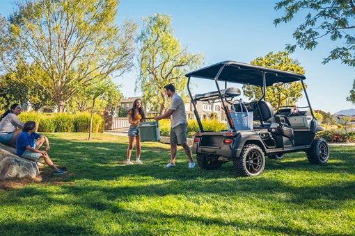 Three-quarter rear angle of a Neighborhood Activity Vehicle parked on grass with a family nearby. opens in a new window