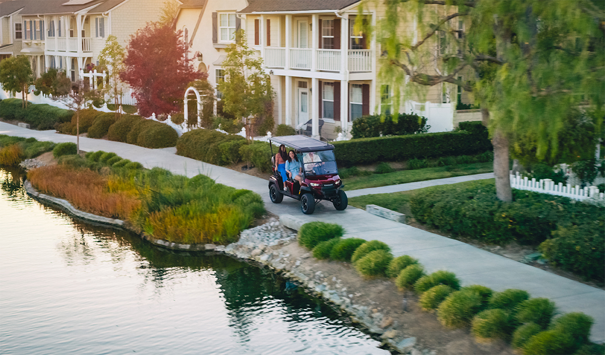 Three-quarter front angle of a family riding in a Neighborhood Activity Vehicle past a pond.
