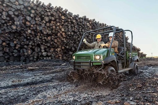 Three-quarter front angle of two people riding a side x side on a jobsite. opens in a new window