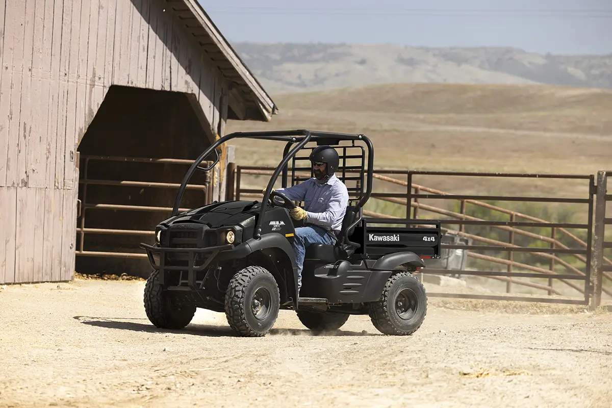Side angle of a person driving a black side x side on a ranch.