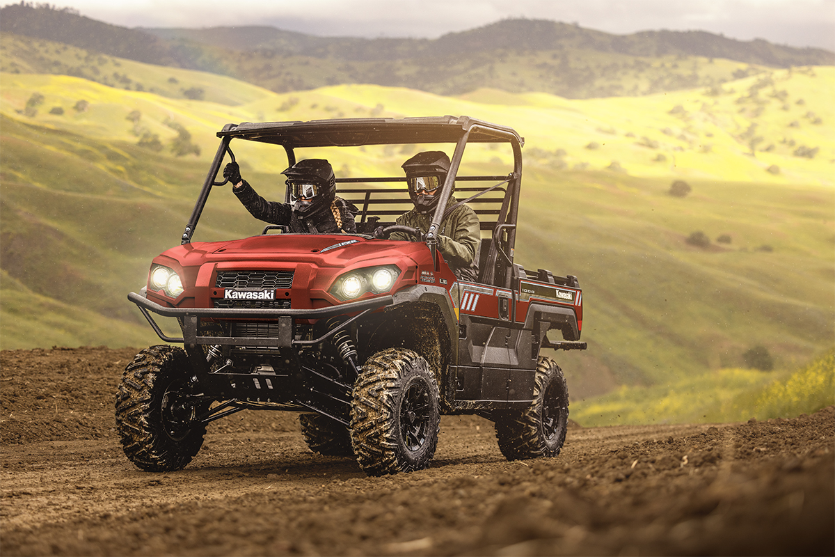 Three-quarter front angle of two people driving a red side x side off-road.