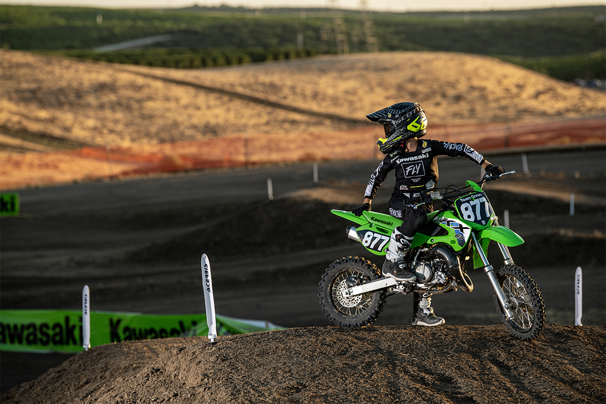 Side angle of a person seated on a motorcycle on a dirt track.