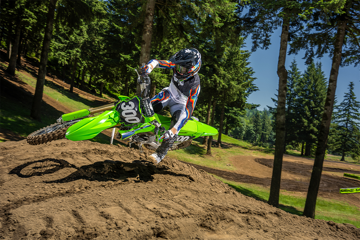 Front angle of a person riding a motorcycle over a small jump on a dirt track.