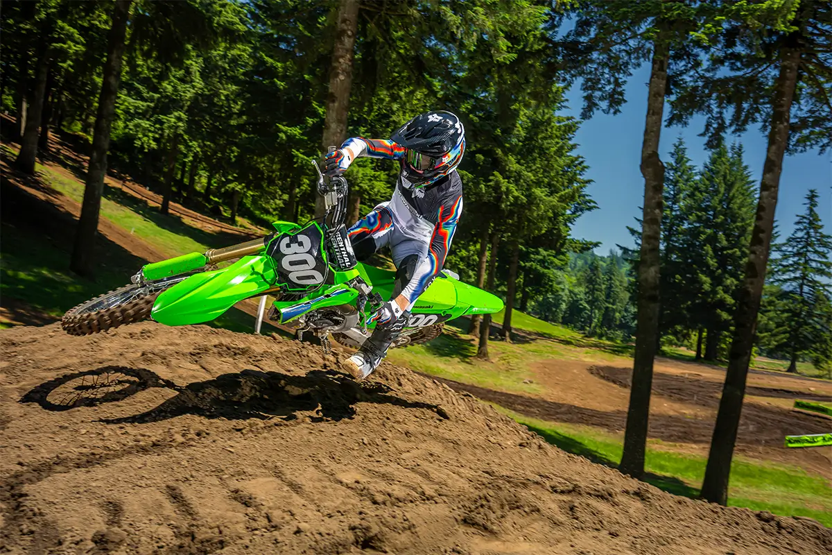 Front angle of a person riding a motorcycle over a small jump on a dirt track.