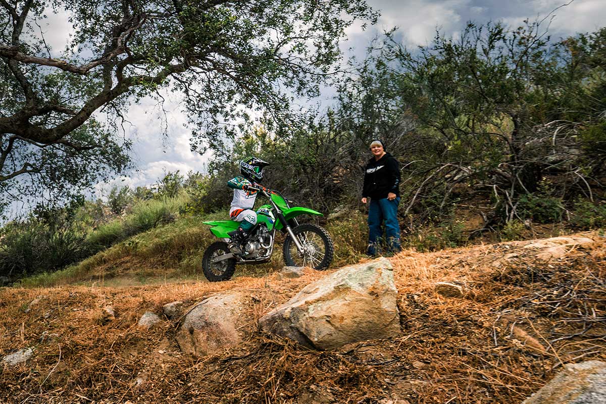 Profile angle of a person riding a motorcycle off-road under adult supervision.