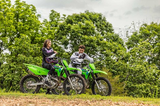 Side angle of two people seated on separate stationary motorcycles off-road. opens in a new window