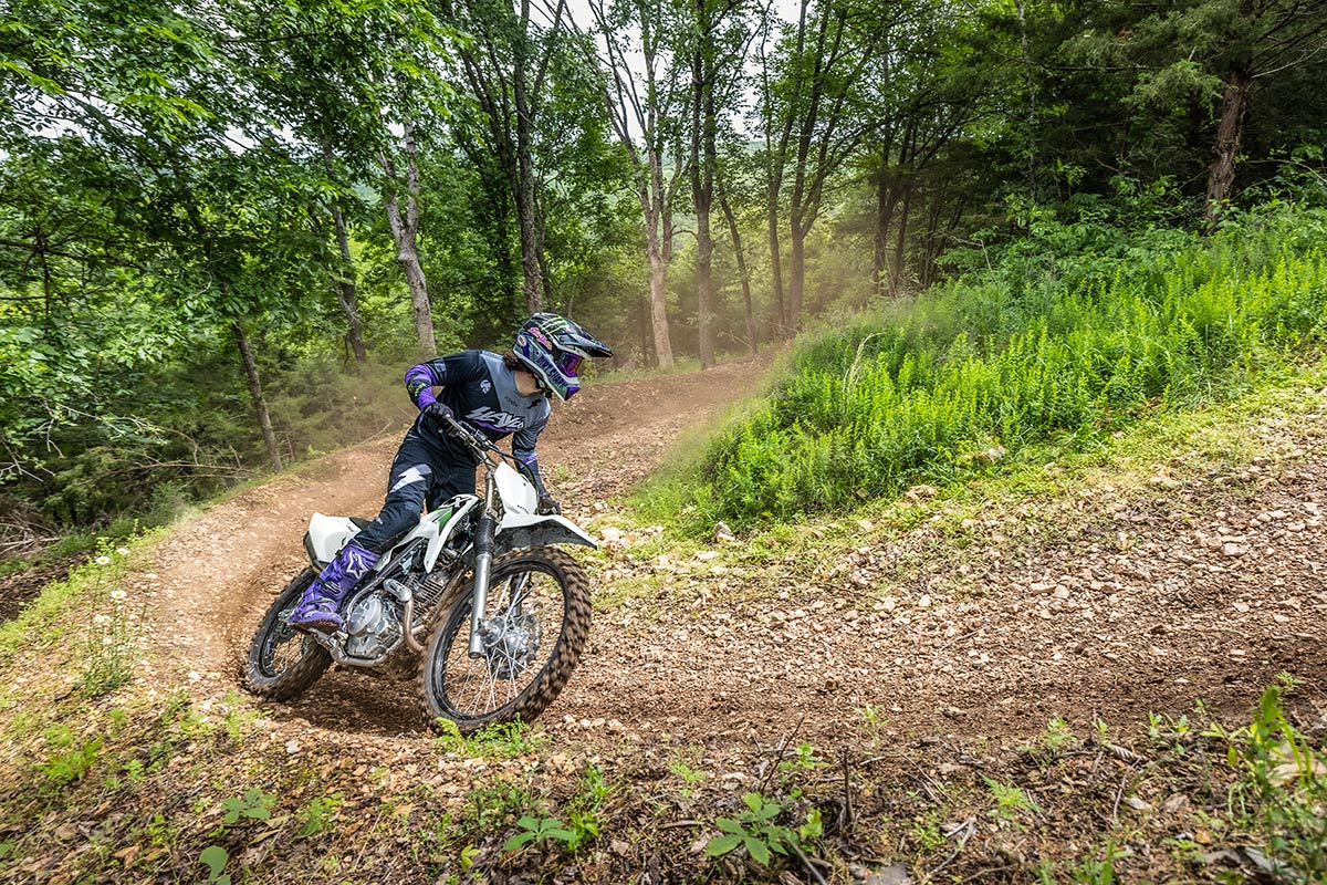 Three-quarter front angle of a person riding a motorcycle around a bend on an off-road course.