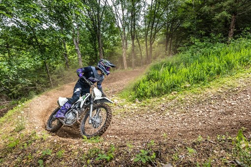 Three-quarter front angle of a person riding a motorcycle around a bend on an off-road course. opens in a new window